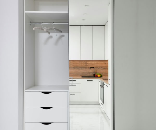 Wardrobe in hallway with mirrored wall reflecting furniture of modern kitchen in light apartment